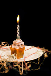 Burning candle on an orange cupcake with decorative icing to celebrate Halloween or a childs birthday