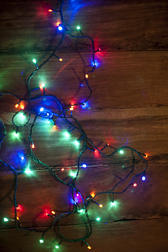 Sparkling garland of colorful Christmas lights lying entwined on a wooden table in a seasonal background, overhead view